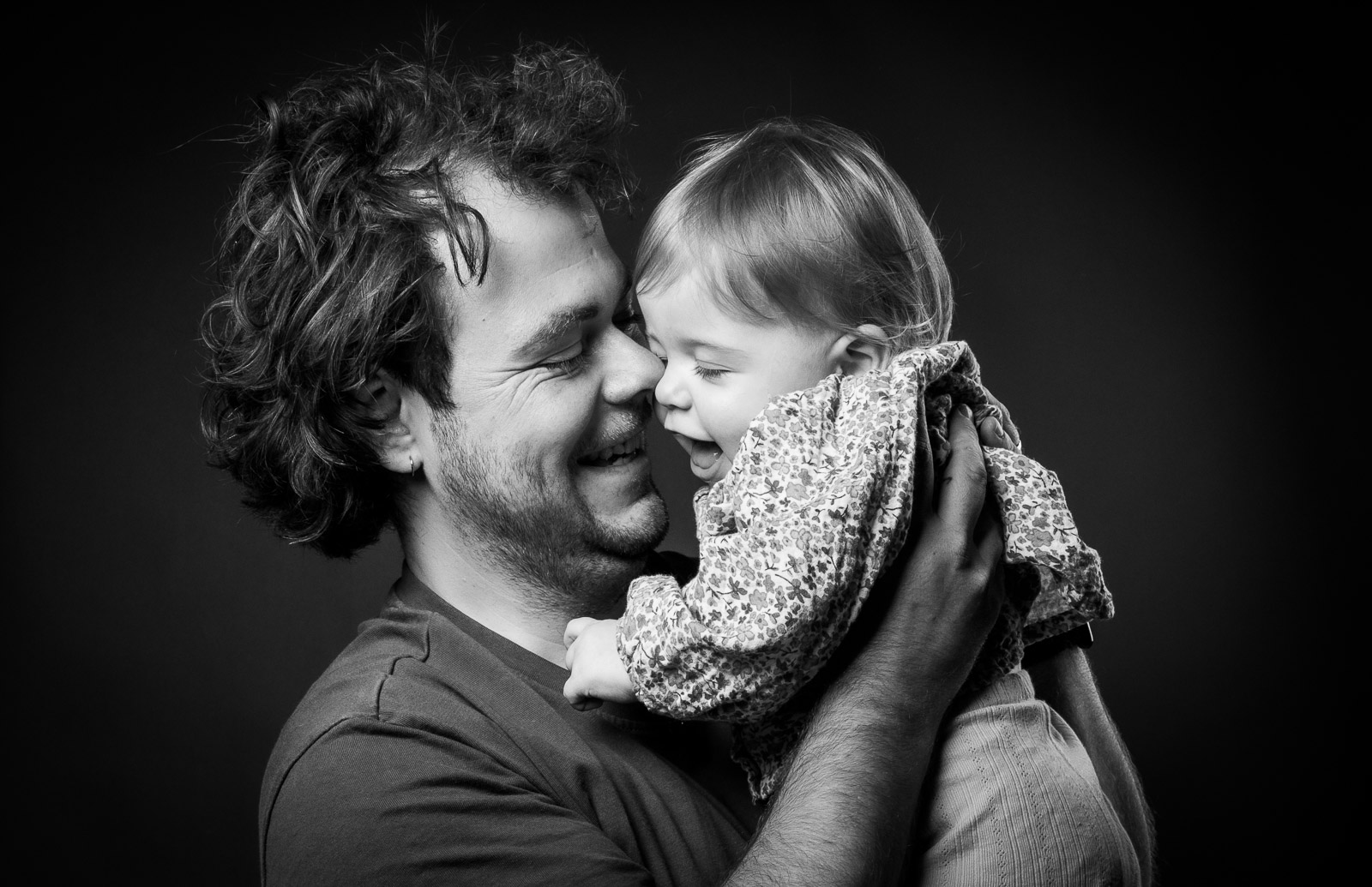 Intiem zwart-wit portret van een lachende vader die zijn vrolijke dochtertje vasthoudt, warme familiefotografie.