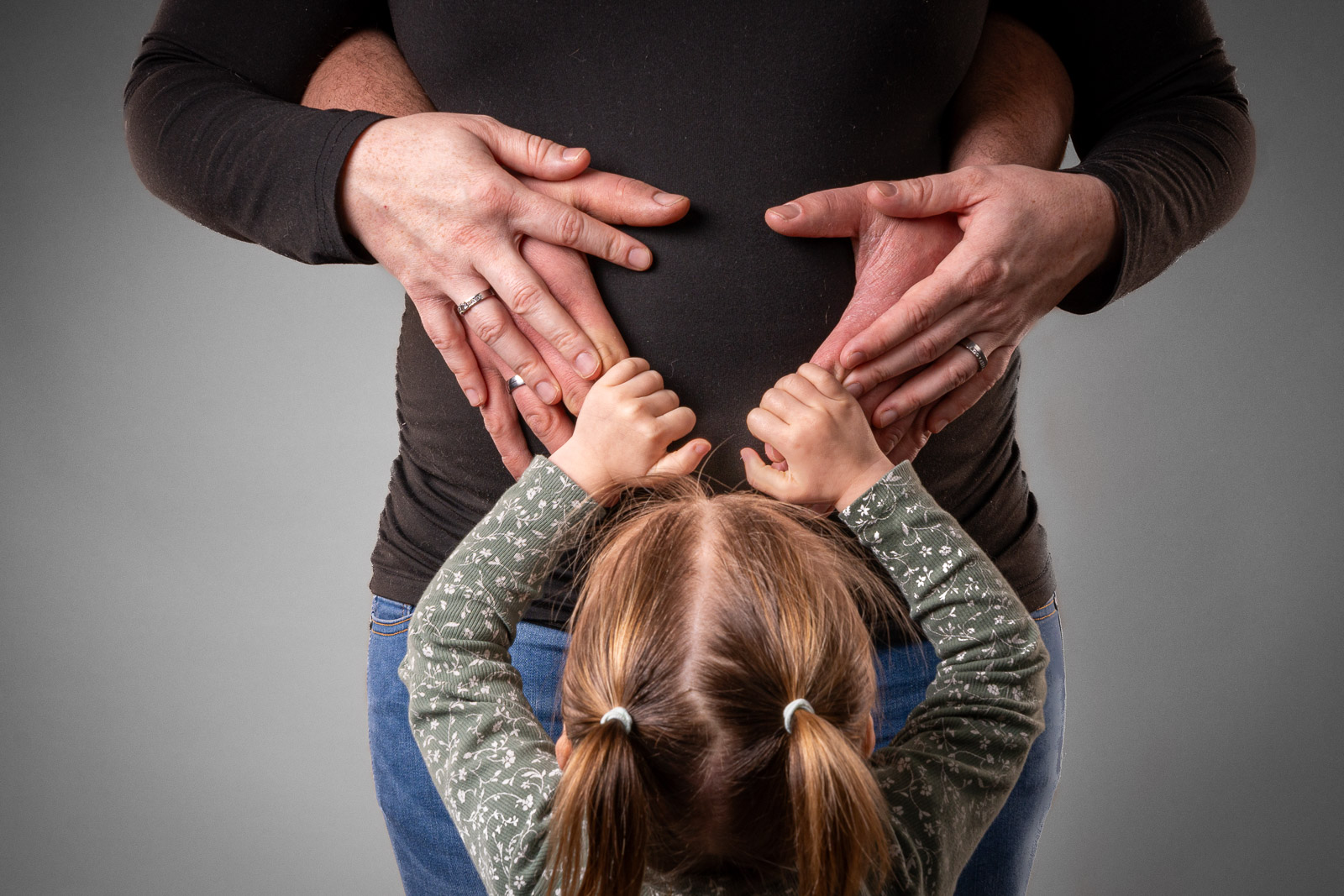 Warme familiefotografie in de studio waarbij handen van ouders en kind liefdevol op een zwangere buik rusten.