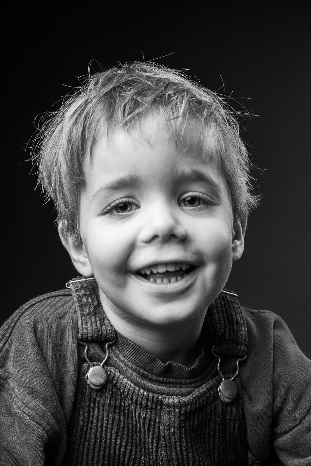 Spontaan zwart-wit kinderportret van een schaterlachende jongen tegen een donkere achtergrond in de fotostudio.